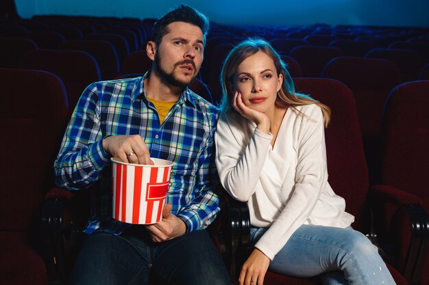영화 극장, 집 또는 영화관에서 영화를보고 매력적인 젊은 백인 부부. 표현력이 풍부하고 놀랍고 감정적으로 보입니다. 혼자 앉아서 즐겁게 지내기. 관계, 사랑, 가족, 주말 시간.