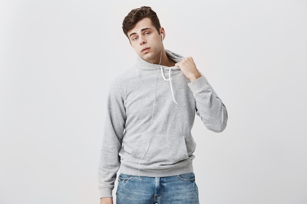 Attractive young caucasian male student in gray hoodie and jeans, puffing out his cheeks, like he is tired of running as he is late for classes.