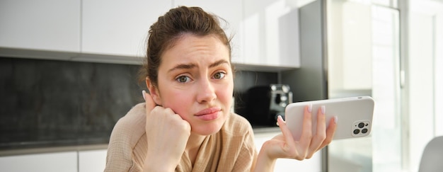 Foto gratuita attraente giovane ragazza allegra che cuoce in cucina preparando un impasto tenendo il ricettario con idee