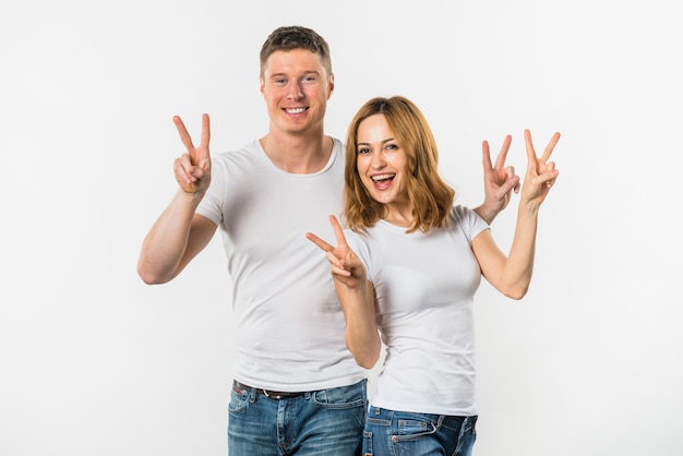 An attractive young couple showing victory sign against white backdrop