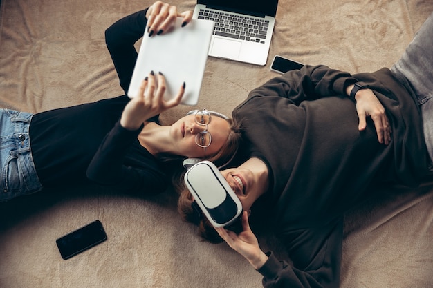 Attractive young couple using devices together, tablet, laptop, smartphone, headphones wireless. Communication, gadgets concept. Technologies connecting people in self-insulation. Lifestyle at home.