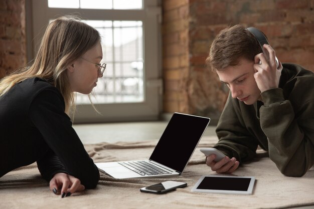 Attractive young couple using devices together, tablet, laptop, smartphone, headphones wireless.