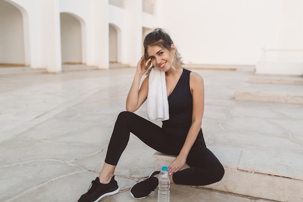 Free photo attractive young cute woman relaxing after workout on white east architecture. fitness, fashionable model, healthy lifestyle, motivation, true positive emotions, smiling