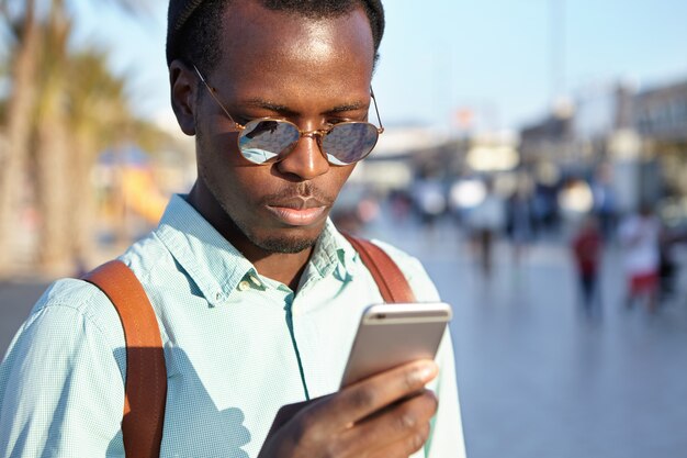 휴대 전화에서 온라인 탐색 응용 프로그램을 사용하여 매력적인 젊은 뭇 남성 관광. 유행 흑인 문자 메시지