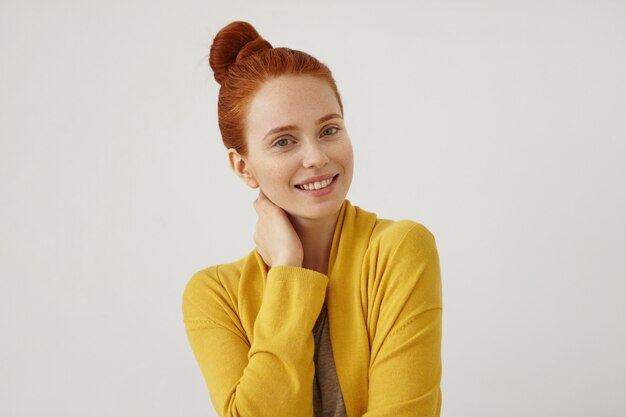 Attractive young female model with ginger hair, wearing yellow cape, keeping her hand on neck, looking with happy expression