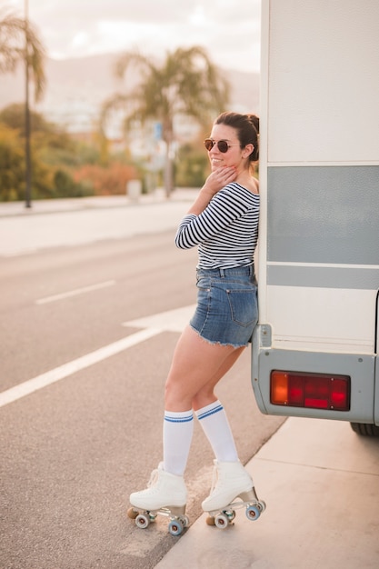 Привлекательная молодая фигуристка склоняется возле каравана на дороге