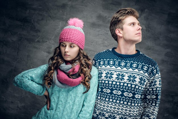 Attractive young female in winter hat and young guy in warm sweater on grey background.