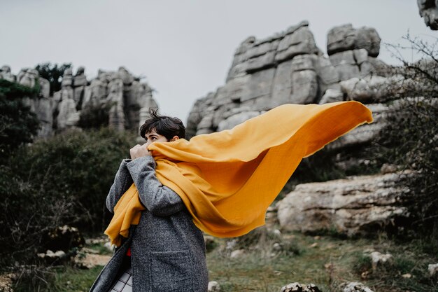 Attractive young female with a coat and a yellow scarf near high rocky cliffs