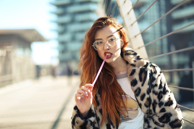 Attractive young female with glasses wearing a coat and chewing a gum