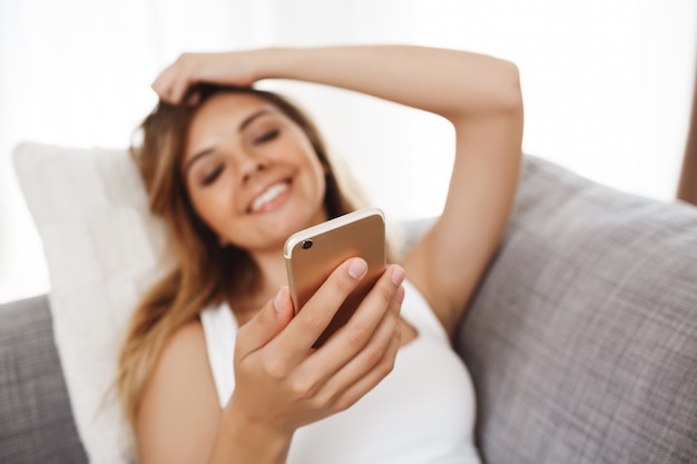 Attractive young girl lying on armchair and chatting at living room