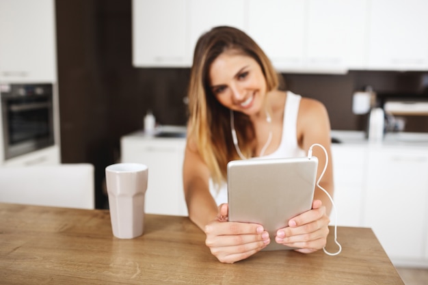 Attractive young girl sitting at dinner table and making selfie with tablet