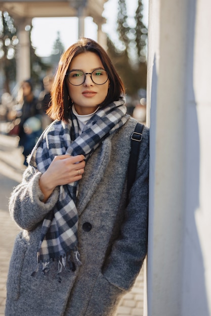 Attractive young girl wearing glasses in a coat walking on a sunny day