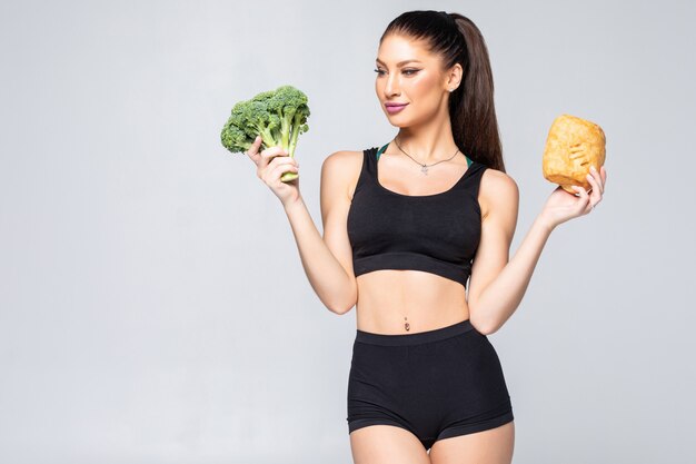 attractive young healthy woman holding an broccoli and a croissant, choosing