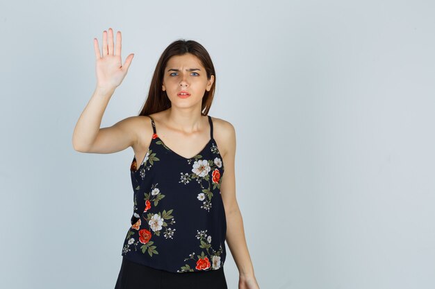 Attractive young lady in blouse showing stop gesture and looking confused , front view.