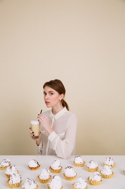 Attractive young lady posing near cupcakes holding coffee