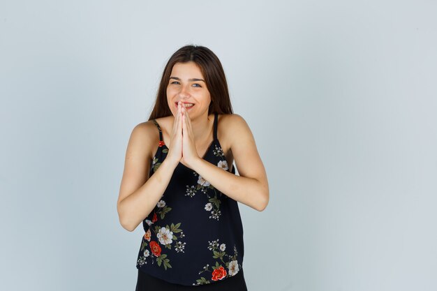 Attractive young lady showing namaste gesture in blouse and looking cheerful , front view.