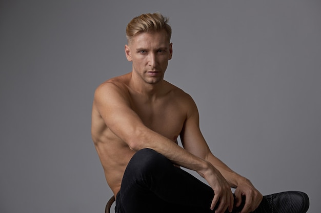 Free photo attractive young man posing with naked torso sitting on a chair