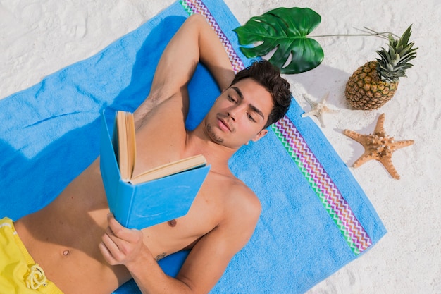 Foto gratuita libro di lettura attraente del giovane sulla spiaggia