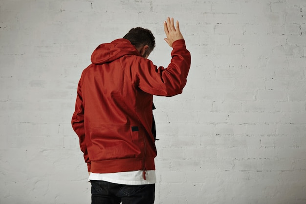 An attractive young man in red jacket waves goodbye portrait from the back on white wall