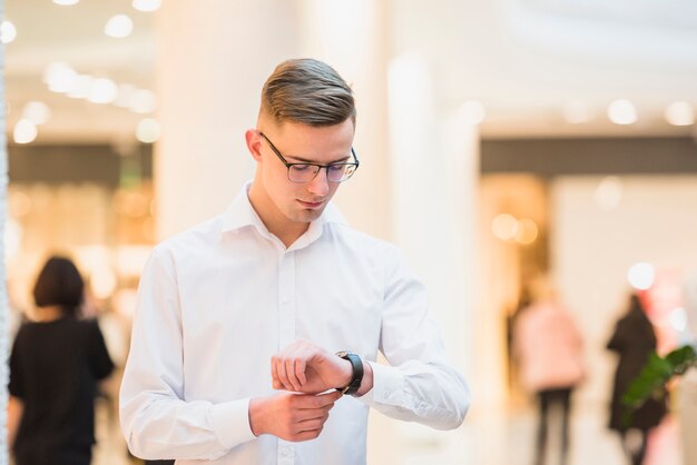 An attractive young man in white shirt looking his wrist watch; checking the time