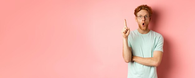 Привлекательный молодой человек с рыжими волосами, поднимающий палец в жесте эврики и подающий идею стоя