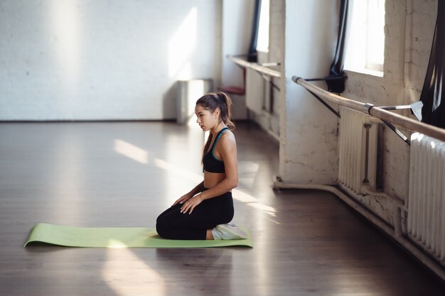 Attractive young woman in activewear choosing healthy lifestyle, sitting on mat. Body shape and activity