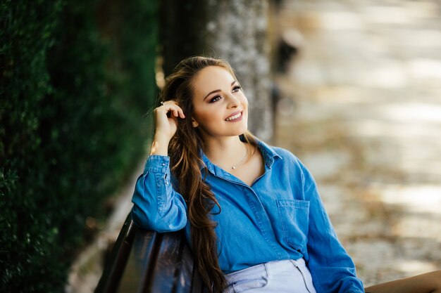 Attractive young woman in black glasses, sitting in a summer park on a bench