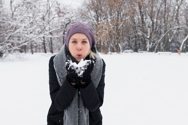 Attractive young woman blowing snow in winter nature