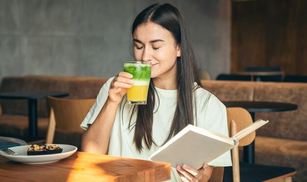 Free photo attractive young woman in a cafe is reading a book with a glass of lemonade