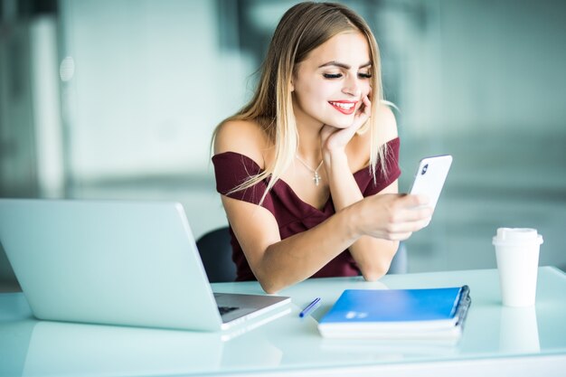 Attractive young woman checking her text messages on her mobile phone with a serious expression as she sits at her desk in the office