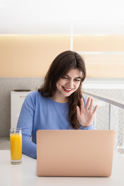 魅力的な若い女性がカフェに座ってビデオ通話で通信