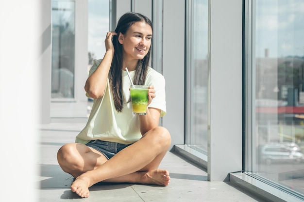 無料写真 窓際に座りながら冷たい飲み物を飲む魅力的な若い女性