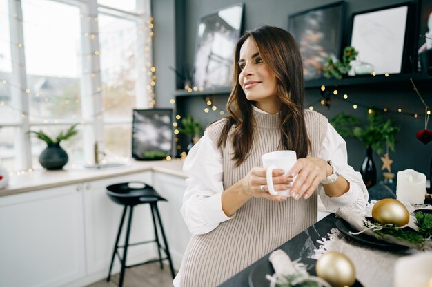 Attraente giovane donna beve il tè in cucina per natale