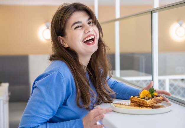 Attractive young woman eats belgian waffles and juice for breakfast