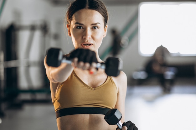 Free photo attractive young woman exercising with dumbbells at the gym