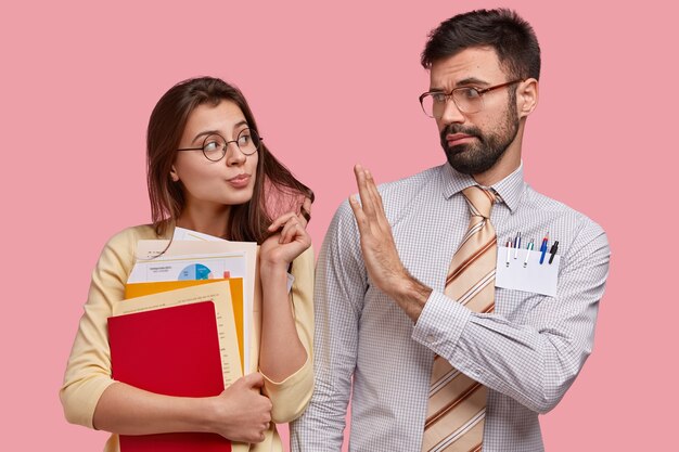 Attractive young woman flirts with handsome male colleague, carries books and documents