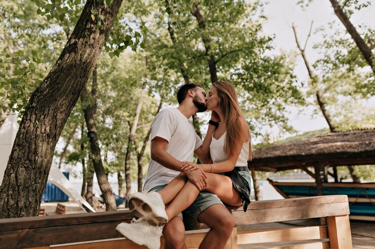 Attractive young woman and handsome man are kissing on the wood bench