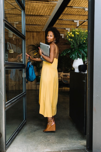 An attractive young woman holding bag and laptop entering in the restaurant