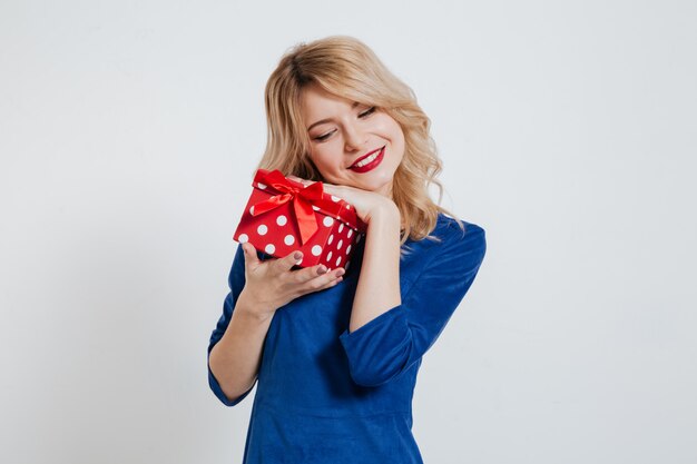 Attractive young woman holding gift box over white wall