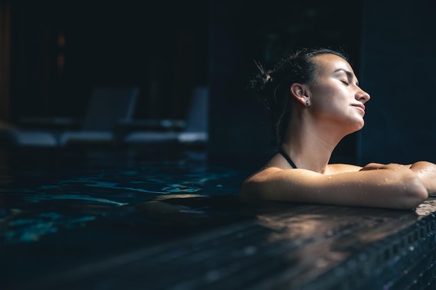 Бесплатное фото Привлекательная молодая женщина в черном купальнике отдыхает в бассейне