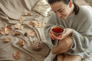 Бесплатное фото Привлекательная молодая женщина пьет чай, сидя в постели среди осенних листьев