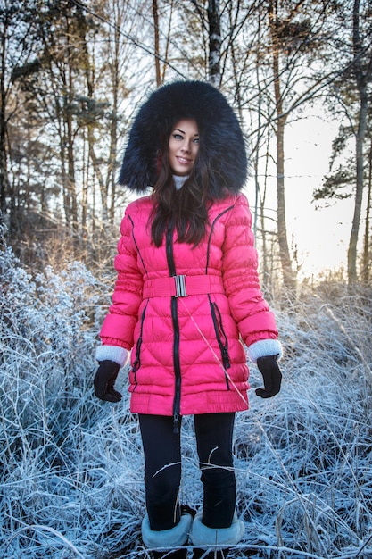 Attractive young woman in pink coat posing in frozen forest.