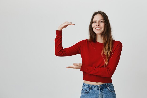 Attractive young woman shaping big object or box with hands, smiling pleased