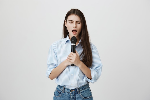 Attractive young woman singing with closed eyes with microphone