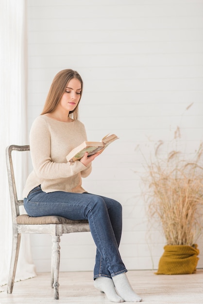 Привлекательная молодая женщина, сидя на деревянном стуле, читая книгу