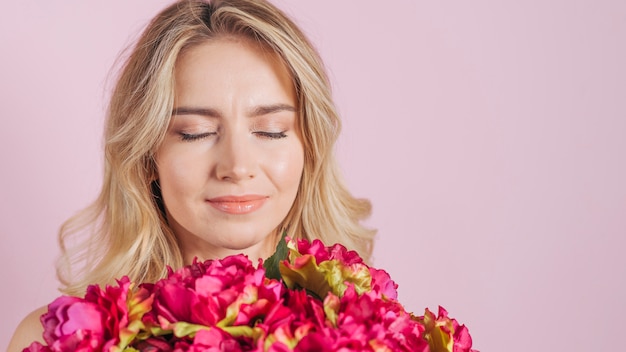 魅力的な若い女性はピンクの背景に対して花の花束の香り