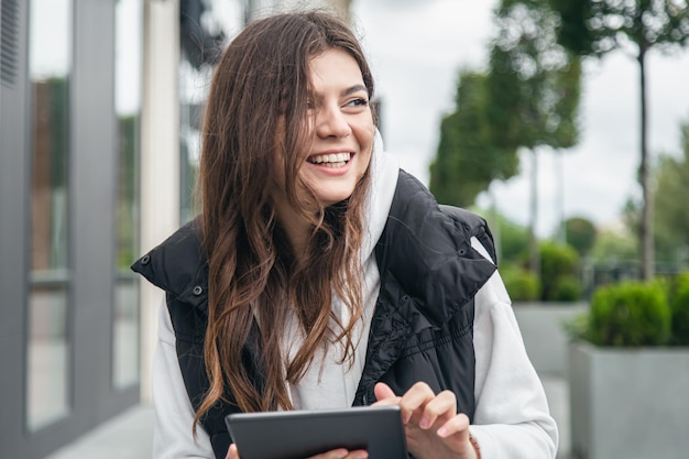 Привлекательная молодая женщина улыбается и использует планшет на улице