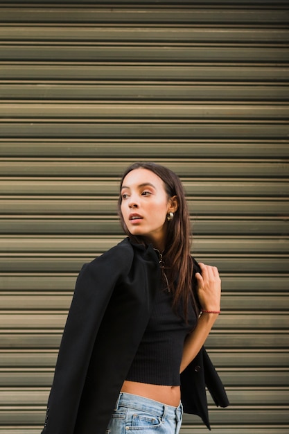 An attractive young woman standing in front of iron shutter looking over shoulder