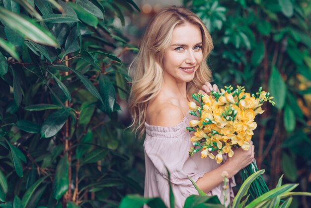 繊細な黄色のフリージアを手に持って植物の近くに立って魅力的な若い女性