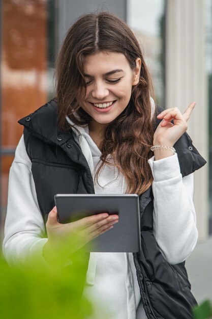 Attractive young woman stands outside and uses a tablet
